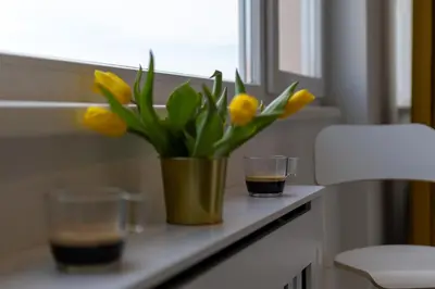 a vase with yellow flowers on a window sill with a drink at Contemporary Vintage, 3BDR Grace Suite in Sofia