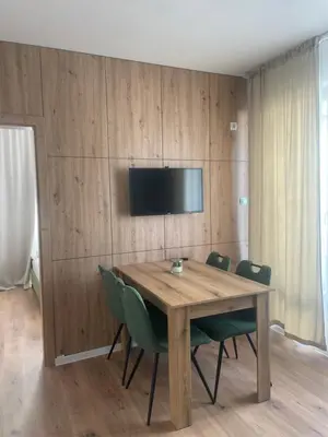 a wooden table with green chairs and a television on a wall at Apartment Park View in Sandanski