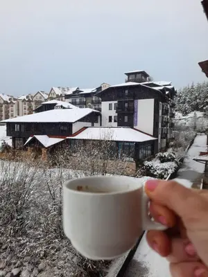 a person holding a cup of coffee on a balcony at Apartment Wintermärchen Bansko in Bansko