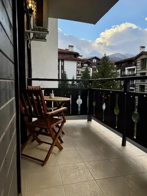 a balcony with a wooden chair and a table at Pirin Cozy Escape 8 min walk from ski lift - Private Apartment Grand Bansko 1 in Bansko