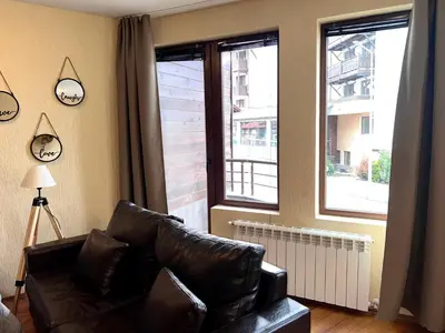 a living room with a leather couch and two windows at Slope nest Bansko in Bansko