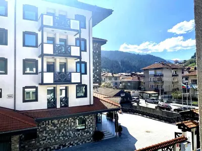 a tall white building with a view of a parking lot at Апартамент и Студио Перелик in Chepelare