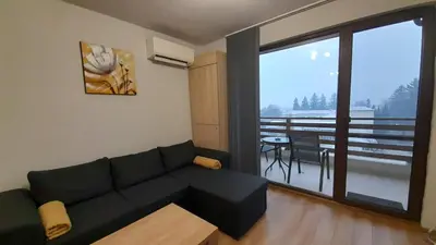 a living room with a black couch and a balcony at Апартамент Славяна in Velingrad