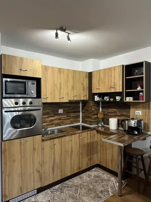 a kitchen with wooden cabinets and a table with a microwave at Двустаен апартамент 