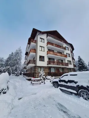 a snow covered building with a car parked in front of it at Rila Park by the Slopes in Borovets