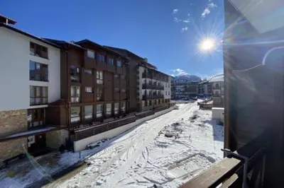 a view of a snowy street with buildings and the sun at Spacious modern 1BR apartment near the gondola in Bansko