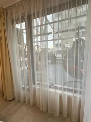 a window with white curtains and a view of a building at Apartment Garden - two large terraces with hanging chairs and sunset view in Sofia