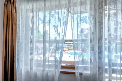 a window with white curtains with a view of a pool at Belvedere Bansko - Cozy 1BR - Ski in Winter, Swim in Summer! by Flat Mаnаger in Bansko