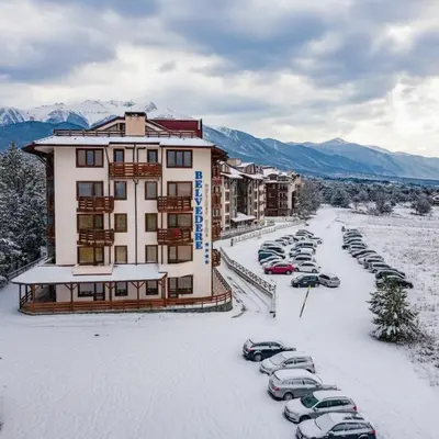 a hotel with cars parked in a parking lot in the snow at Alpine Escape Bansko in Bansko