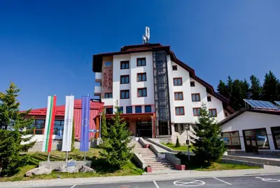 a large white building with flags in front of it at Hotel Coop Rozhen in Pamporovo