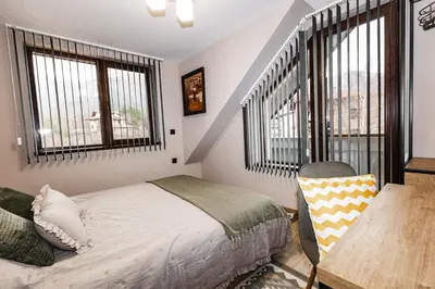 a bedroom with a bed and a desk and windows at Вила Тих кът in Resilovo