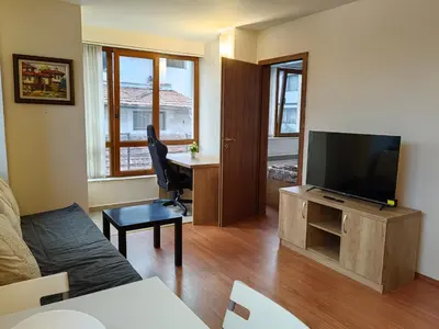 a living room with a television and a desk with a chair at Апартамент Мария in Bansko