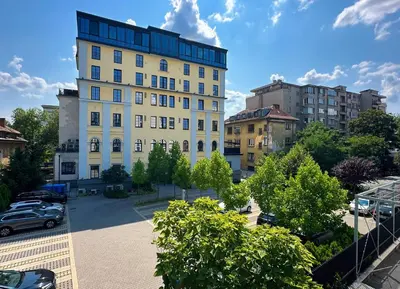 a large white building in a parking lot with cars at 2BR, 4 Baths, Terrace Steps from Sofia Landmarks in Sofia