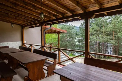 a porch with tables and chairs and a view of the forest at Комплекс Родопска среща - Къщи и Апартаменти in Batak