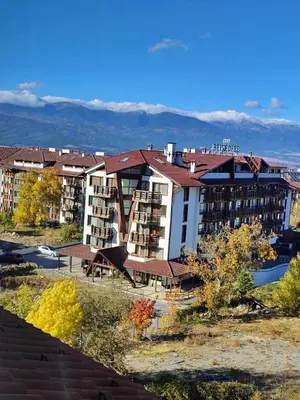 a hotel with a large building with mountains in the background at Bansko Tower Cozy Studio with Mountain View in Bansko