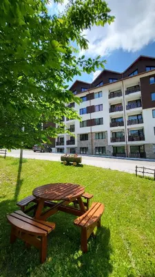 a picnic table and two benches in the grass in front of a building at Private studio B27 in Borovets Gardens in Borovets