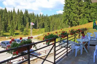a woman sitting at a table on a balcony with flowers at Edelweiss Mountain Apartment - Stream Resort Spa & Pool, Pamporovo in Pamporovo