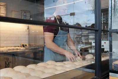 a woman is making bread in a bakery window at Sunny Penthouse with Mountain Views and 180 degrees Terrace in Sofia