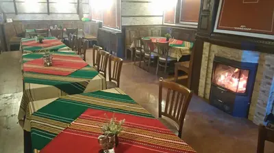 a restaurant with tables and a fireplace in the middle at Guest House H Dzhogolanov in Koprivshtitsa