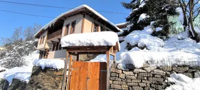 a house with a wooden door in the snow at Chepelare Holiday Guest House in Chepelare
