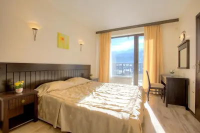 a bedroom with a bed and a desk and a window at Къщи за гости КООП Добринище - Holiday Villages COOP Dobrinishte in Dobrinishte