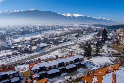 a town covered in snow with mountains in the background at Къщи за гости КООП Добринище - Holiday Villages COOP Dobrinishte in Dobrinishte