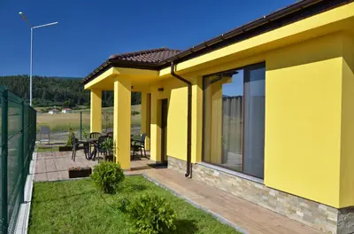 a yellow house with a deck with a patio at Guest House Colori in Tsigov Chark