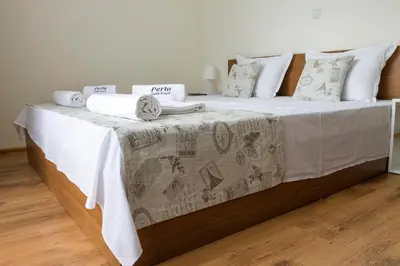 a bed with a white blanket and pillows on it at Хотел PERLA in Strelcha