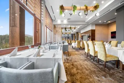 a restaurant with white tables and chairs and large windows at Hotel Orlovetz in Pamporovo