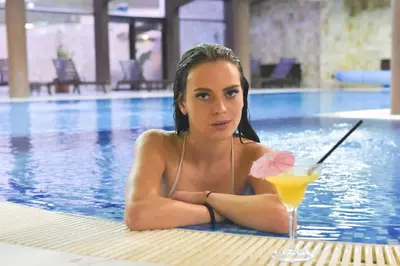 a woman in a swimming pool with a drink at Royal Bansko Family Apart Hotel - All Inclusive Light or Half Board & Drinks With Heated Indoor Pool & Jacuzzis in Bansko