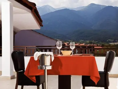a table with wine glasses on a balcony with mountains at Parklands Hotel & Pool in Bansko