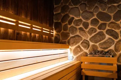 a sauna with a stone wall and a wooden bench at Maxi Park Hotel & Spa in Velingrad