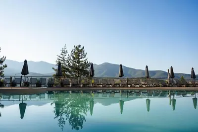 a swimming pool with chairs and umbrellas and mountains at Maxi Park Hotel & Spa in Velingrad