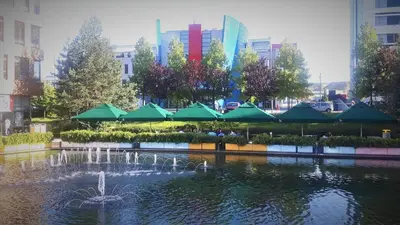 a fountain in a pond with green umbrellas in a city at Business Park Apartment in Sofia