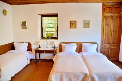 two beds in a room with a table and a window at Kalinia Guesthouse B&B in Kovachevitsa