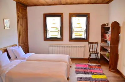 two beds in a room with two windows and a chair at Kalinia Guesthouse B&B in Kovachevitsa
