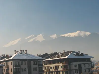 a group of buildings with snow covered mountains in the background at Bariakov Family Hotel in Bansko