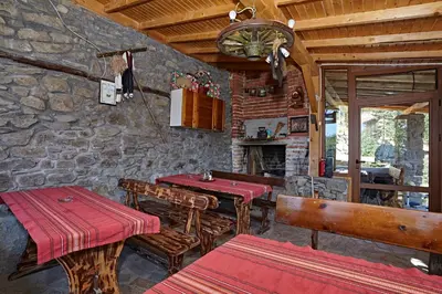a restaurant with a table and benches and a stone wall at Guesthouse Vazrozhdenski kashti in Manastir