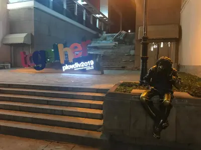 a statue of a man sitting on a ledge in front of a sign at Къща Стария град in Plovdiv