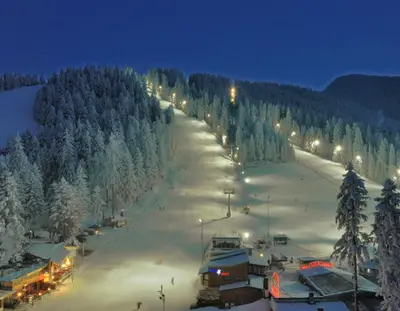 a snow covered ski slope with trees and lights at Enjoy Studios and Lovely Apartment Villa Park in Borovets