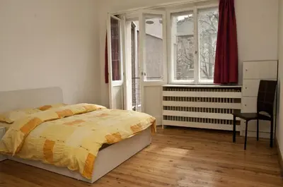 a bedroom with a bed and a chair and windows at Hostel Mostel Sofia in Sofia
