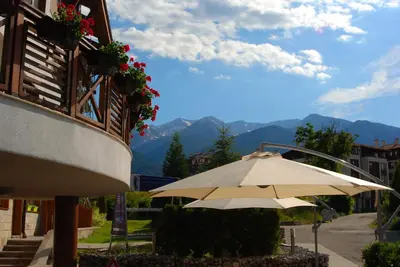 an umbrella sitting next to a building with mountains at White Lavina - Ski, Bike, Hike in Bansko