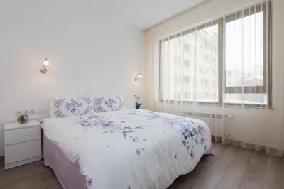 a white bedroom with a large bed with flowers on it at Grand Vitosha Apartments in Sofia