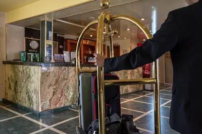 a man in a suit is holding a gold luggagecart at Hotel Montecito in Sofia