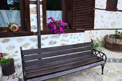 a wooden bench sitting in front of a building with flowers at Family Hotel Dinchova kushta in Rozhen