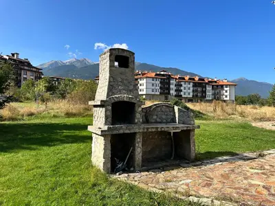 a stone oven sitting in the grass with buildings in the background at White Wood Lodge in Bansko