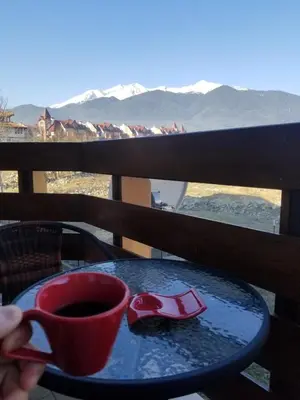 a person holding a cup of coffee on a table with a view at Belveder Holiday Club Private in Bansko