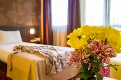 a vase filled with yellow and pink flowers next to a bed at Hotel Villa Boyana - Free Parking in Sofia