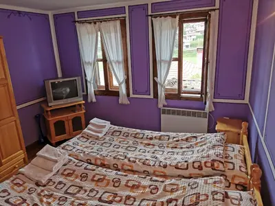 two beds in a bedroom with purple walls and a tv at Hadji Neikovi Guest Houses in Koprivshtitsa