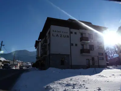 a building in the snow with the sun behind it at Family Hotel Lazur in Bansko